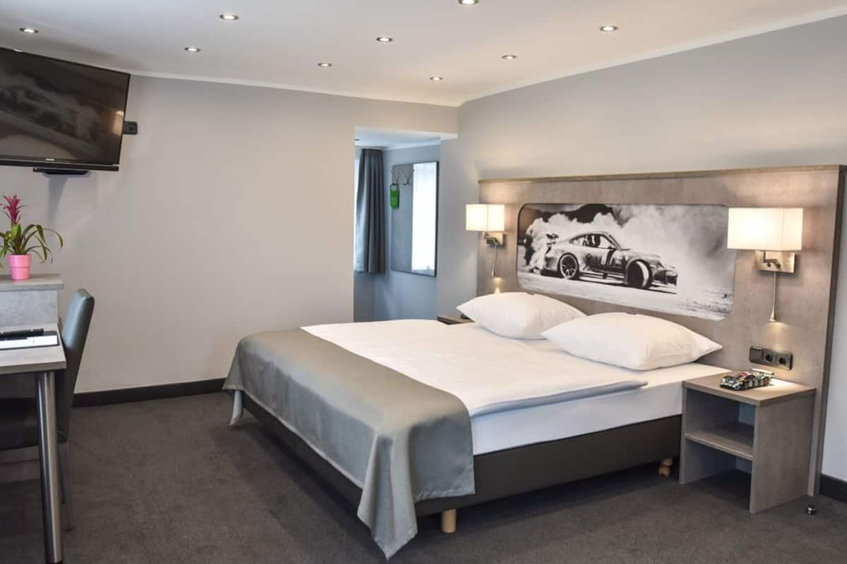 Een moderne hotelkamer met een groot bed, bedlampen, een flatscreen televisie, een bureau met stoel en een potplant.