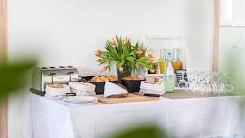 Una mesa de buffet con pan, bollería y un jarrón de tulipanes.