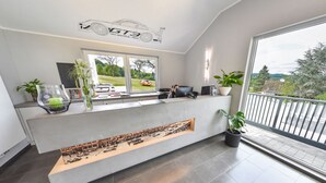 A modern reception desk with a cityscape photograph, a car model, and a balcony with a view of trees and a distant landscape.