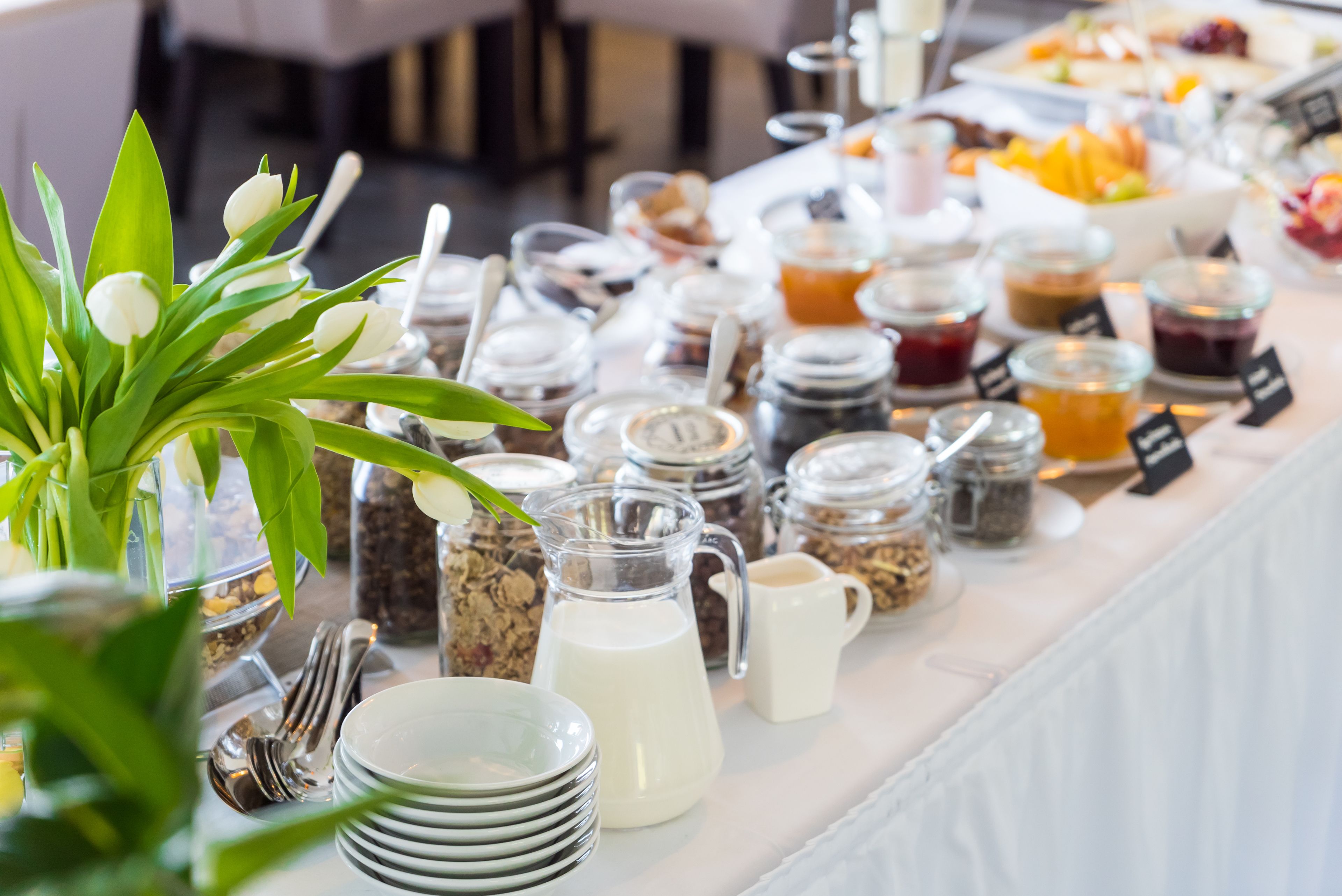 A buffet table with various food items, including fruits, pastries, and beverages, arranged on a white tablecloth.