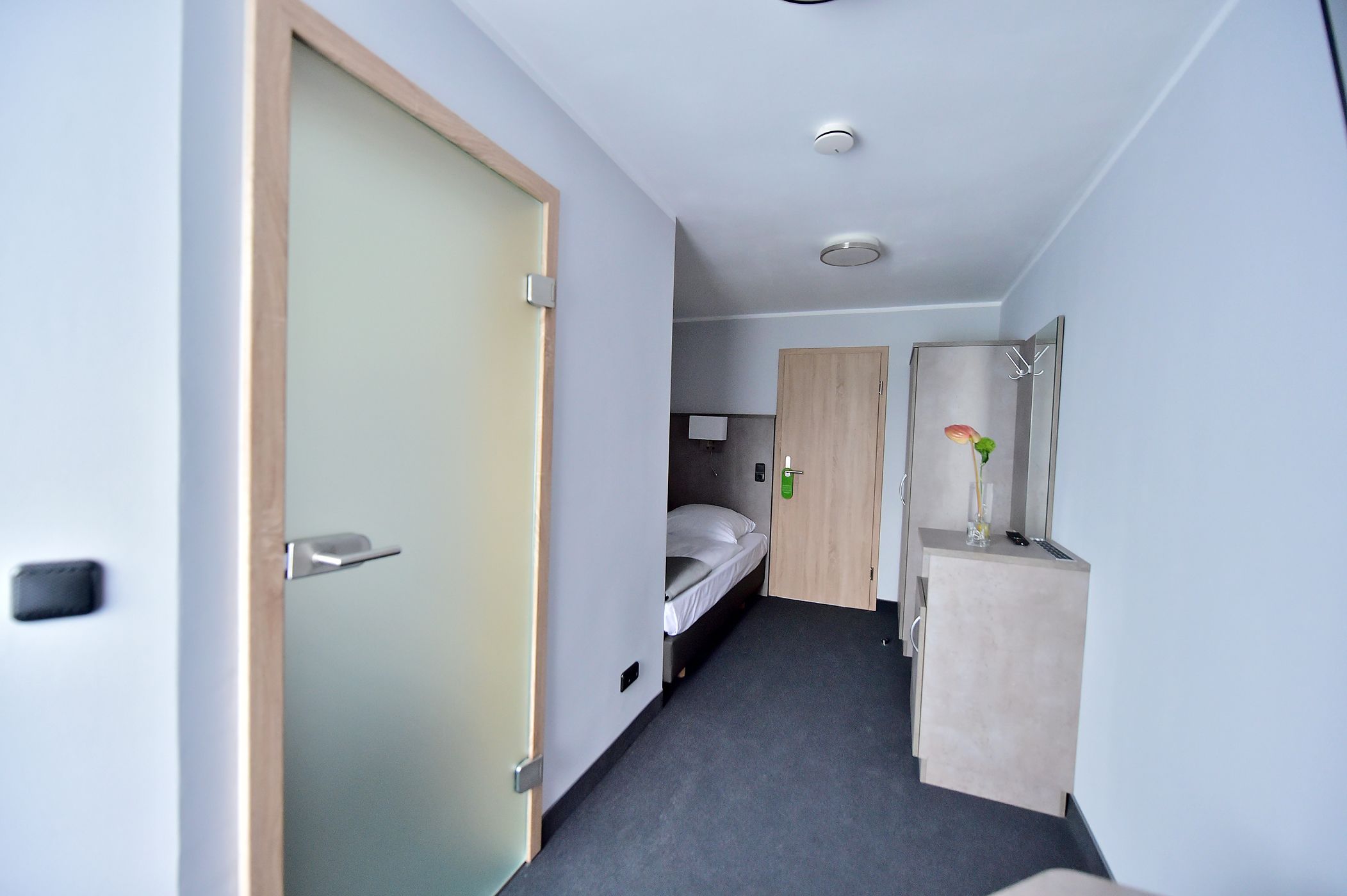 Un couloir étroit avec un lit, un petit bureau et un miroir.