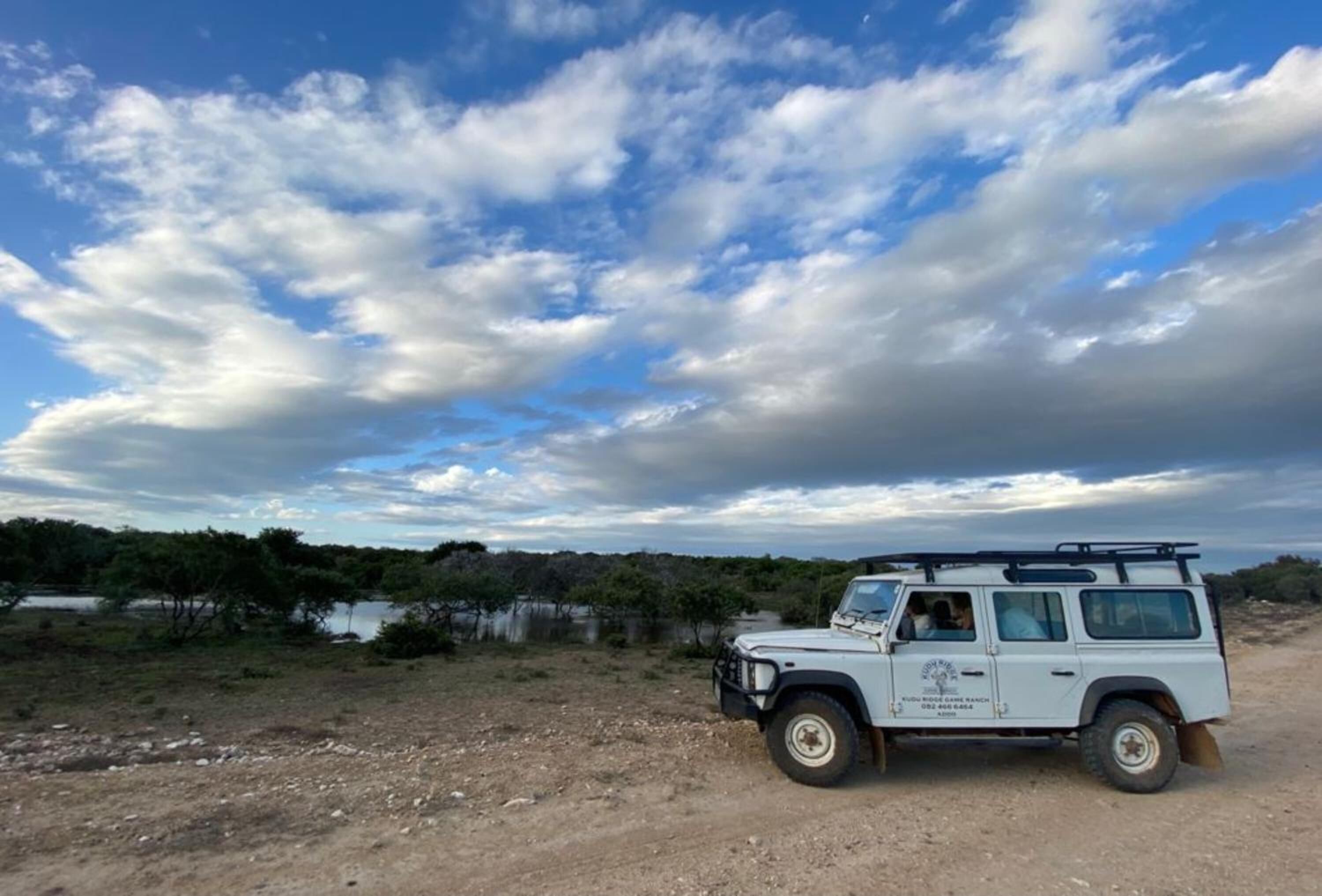 A white off-road vehicle parked on a dirt road with a lake and trees in the background.