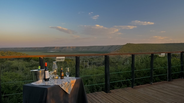 A table with bottles and glasses on a wooden deck overlooking a valley.