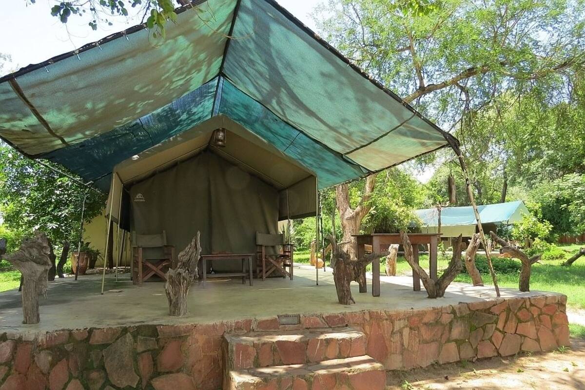 A tented outdoor area with a stone platform, wooden benches, and a table under a large shade structure.