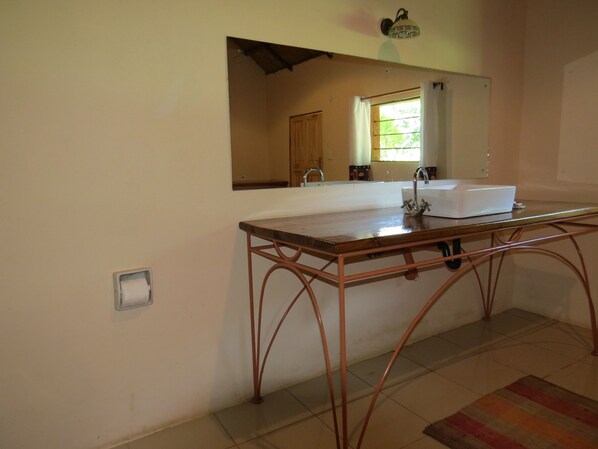 Un baño con tocador de madera, lavamanos y espejo.