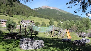 A playground with a rope swing, a slide, and large rocks. - Hotel Al Rom (Val Muestair)