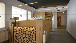 A reception area with a wooden log display, a glass vase with a candle, and a wooden counter. - Hotel Al Rom (Val Muestair)