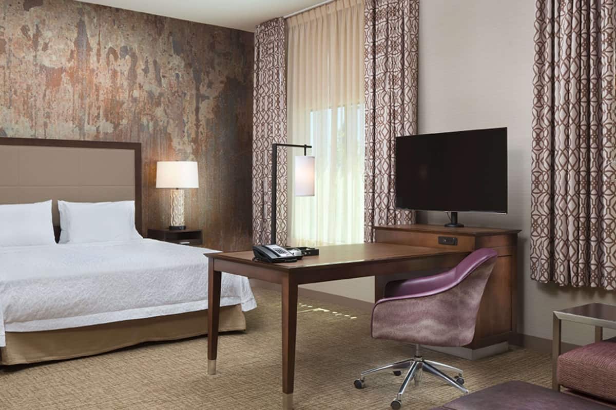 A hotel room with a bed, desk, chair, television, and a small table.