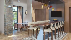 A modern dining area with a long wooden table, multiple chairs, and pendant lighting. - Hampton Inn & Suites Murrieta Temecula (Murrieta)