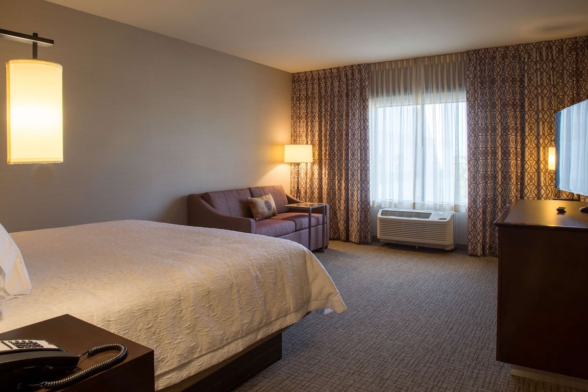 A hotel room with a large bed, a desk with a telephone, a sofa, and a TV.
