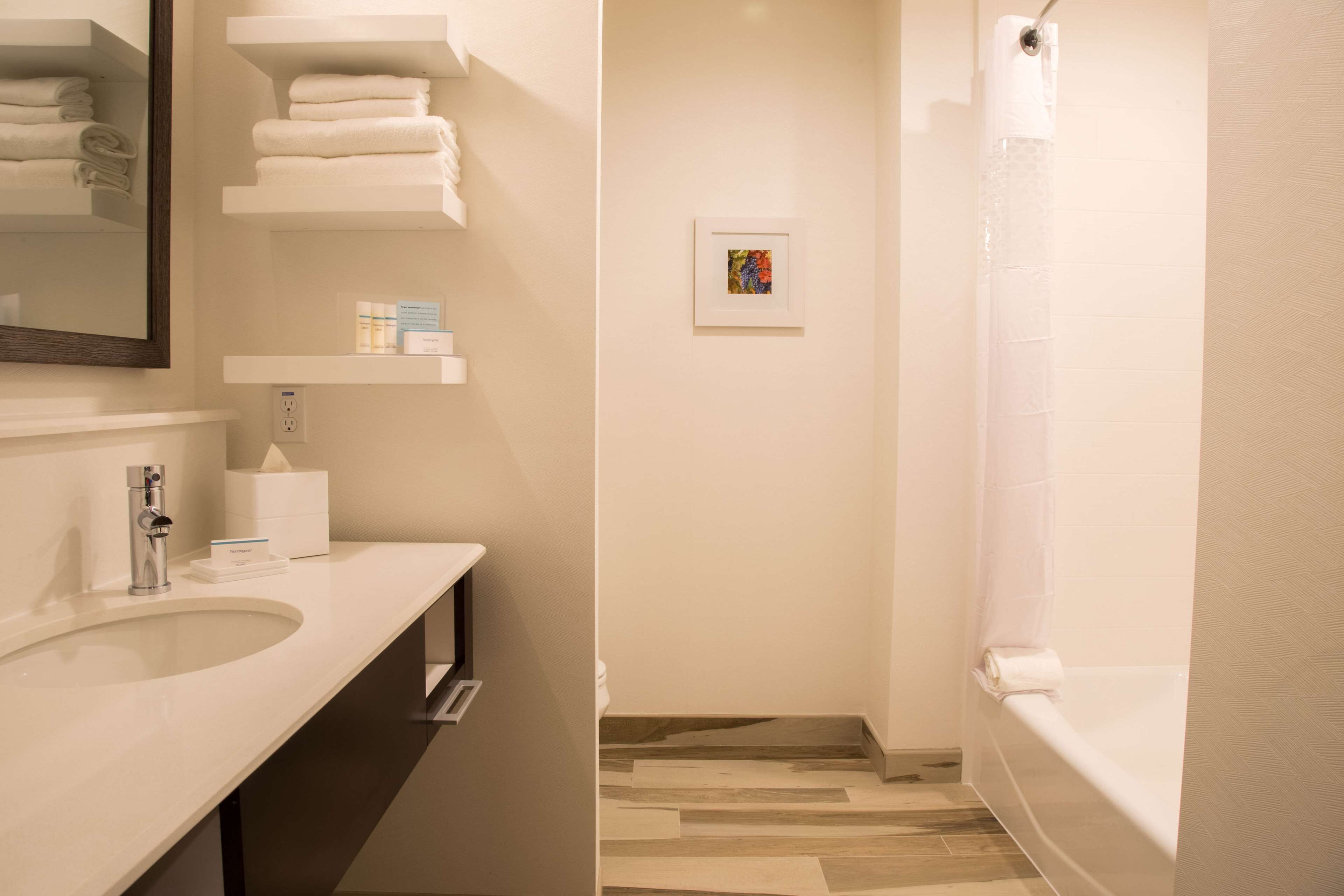 Ein modernes Badezimmer mit Waschbecken, Spiegel, Handtuchhaltern und einer Dusche.