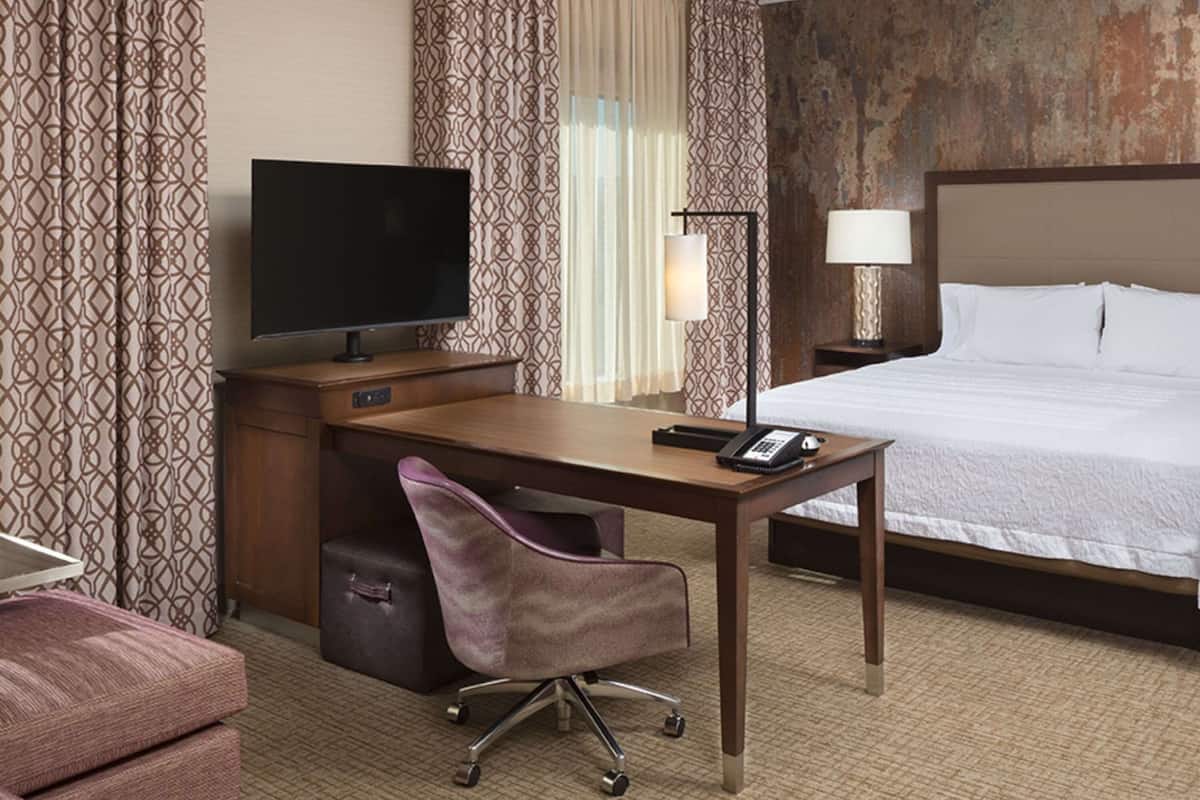 A hotel room with a bed, a desk with a computer, a chair, a TV, and a lamp.