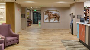 A hotel reception area with a wooden floor, a reception desk, a large wall-mounted artwork of a horse, and a purple armchair. - Hampton Inn & Suites Murrieta Temecula (Murrieta)