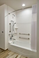 A modern bathroom with a bathtub, shower, and handrails.