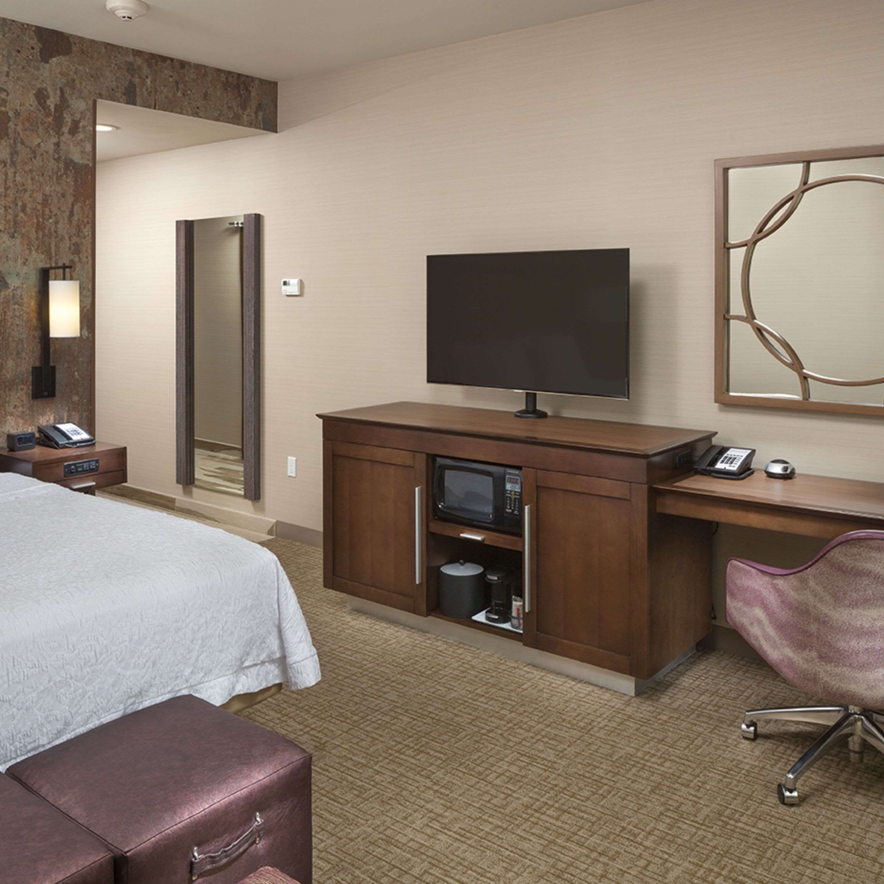 A hotel room with a bed, a desk with a television, a chair, and a suitcase.
