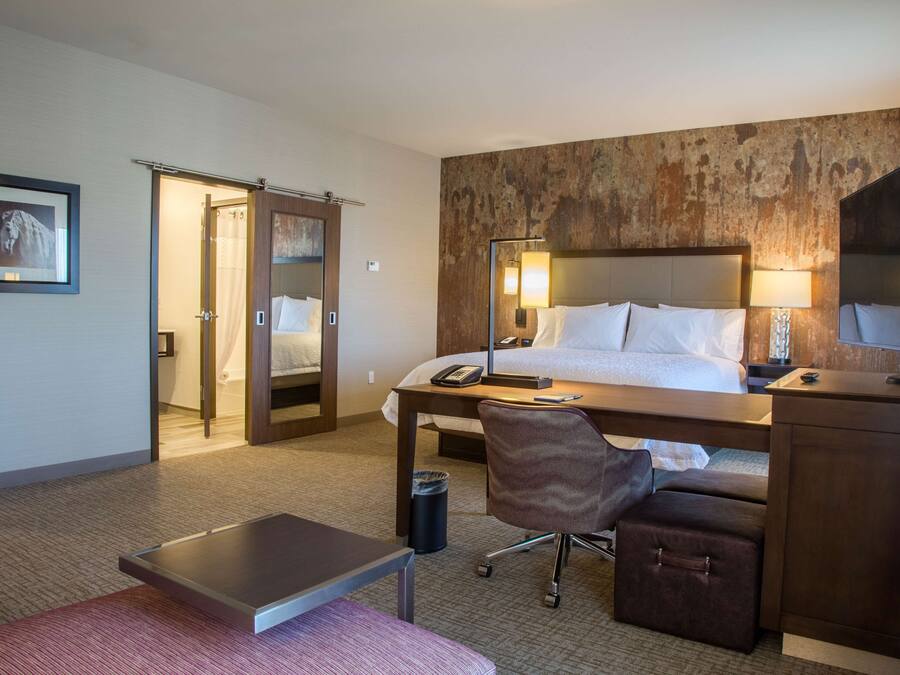 Hotelkamer met een bed, bureau, stoel en een kleintje tafel. Er hangt een spiegel boven het bureau en een schilderij aan de muur.