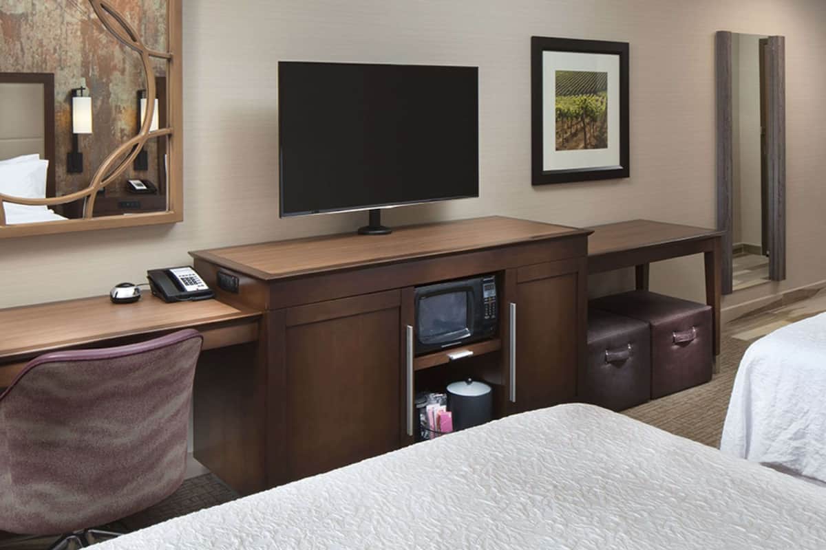 A hotel room with a bed, a desk with a computer, a telephone, a microwave, and a television.