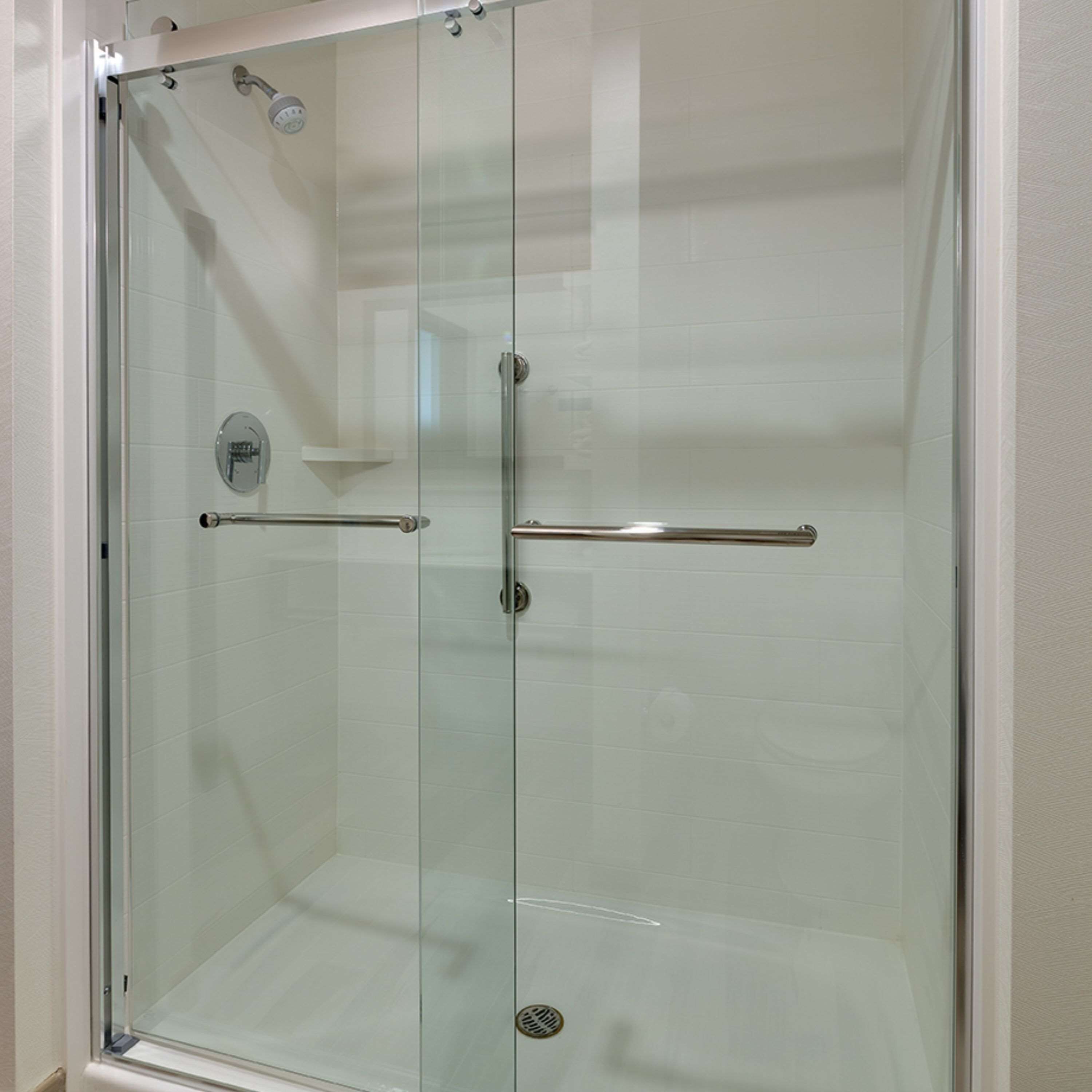 A glass-enclosed shower stall with a handheld showerhead, a handheld shower control, and a safety bar.