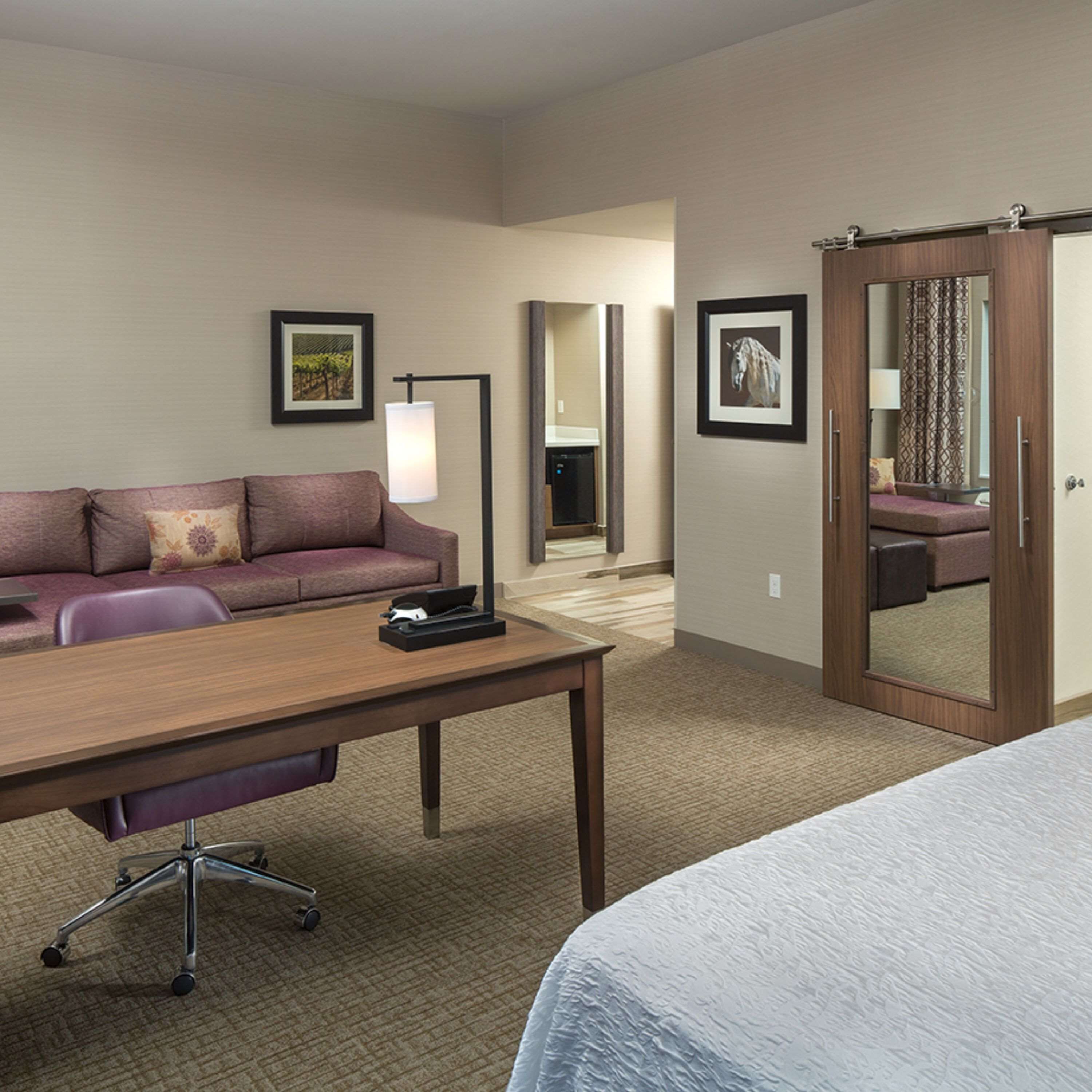 Una habitación de hotel con sofá, escritorio, lámpara, cama y espejo.
