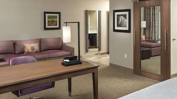 Una habitación de hotel con sofá, escritorio, lámpara, cama y espejo.