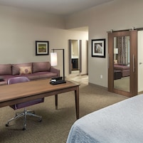 Una habitación de hotel con sofá, escritorio, lámpara, cama y espejo.