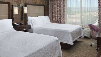 A hotel room with two beds, a desk, a chair, and a large window with curtains.