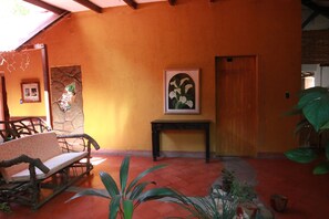 A room with a wooden bench, a stone wall with a picture, a wooden door, and a potted plant. - Hotel La Tora (Managua)
