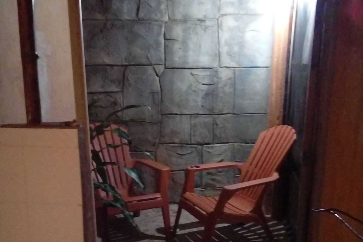 A narrow corridor with a stone wall, two wooden chairs, and a tiled floor.