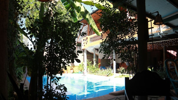 Ein Poolbereich mit einem Steinweg, umgeben von Grünflächen und einem Gebäude mit Balkon.