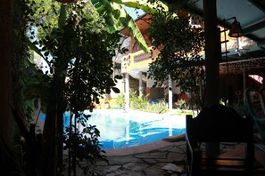 A pool area with a stone pathway, surrounded by greenery and a building with a balcony. - Hotel La Tora (Managua)