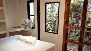 Ein Schlafzimmer mit Bett, Ventilator und Blick auf einen Garten durch eine Glastür.