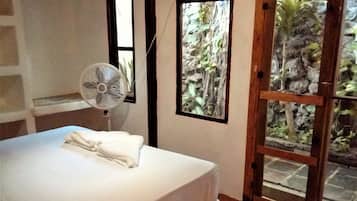 Un dormitorio con cama, ventilador y vistas a un jardín a través de una puerta de cristal.