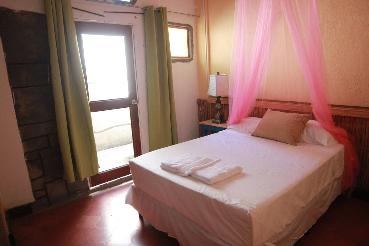 A bedroom with a bed, curtains, a nightstand, a lamp, and a window.
