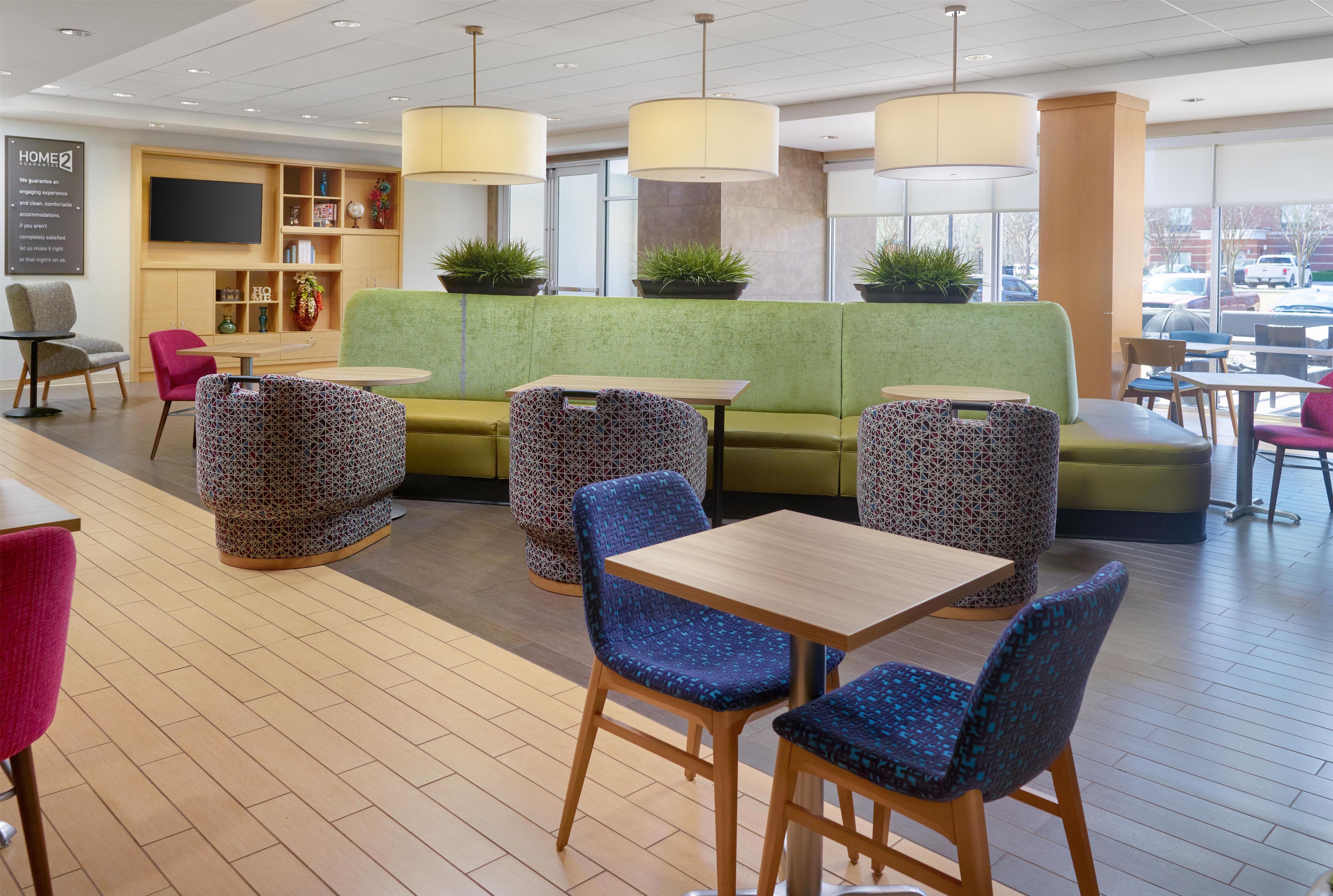 A modern hotel lobby with a green sofa, patterned chairs, and tables.