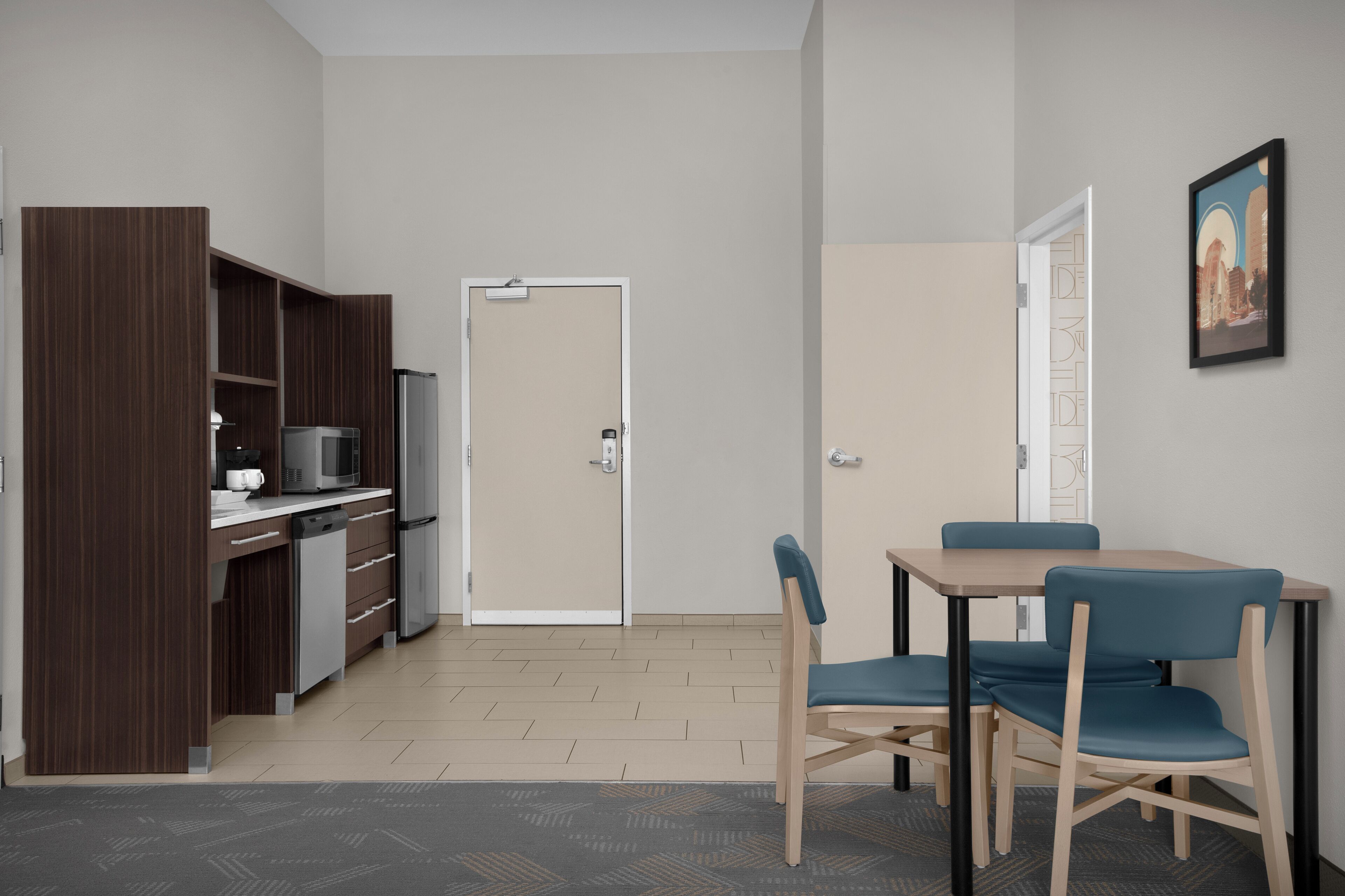 Una cocina moderna con microondas, cafetera y armarios, un comedor con mesa y sillas, y una puerta que conduce a otra habitación.