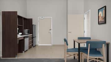 Una cocina moderna con microondas, cafetera y armarios, un comedor con mesa y sillas, y una puerta que conduce a otra habitación.