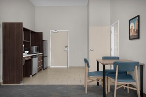 Una cocina moderna con microondas, cafetera y armarios, un comedor con mesa y sillas, y una puerta que conduce a otra habitación.