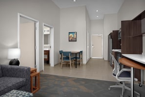 Een moderne hotelkamer met een bank, een klein tafeltje, een bureau en een stoel. Er is een deur naar een badkamer en een gang.