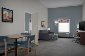 Een kamer met een tafel en stoelen, een bank, een televisie en een raam met gordijnen met een patroon.