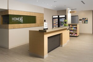 Zona de recepción de un hotel con un mostrador, un refrigerador y una estantería con aperitivos.