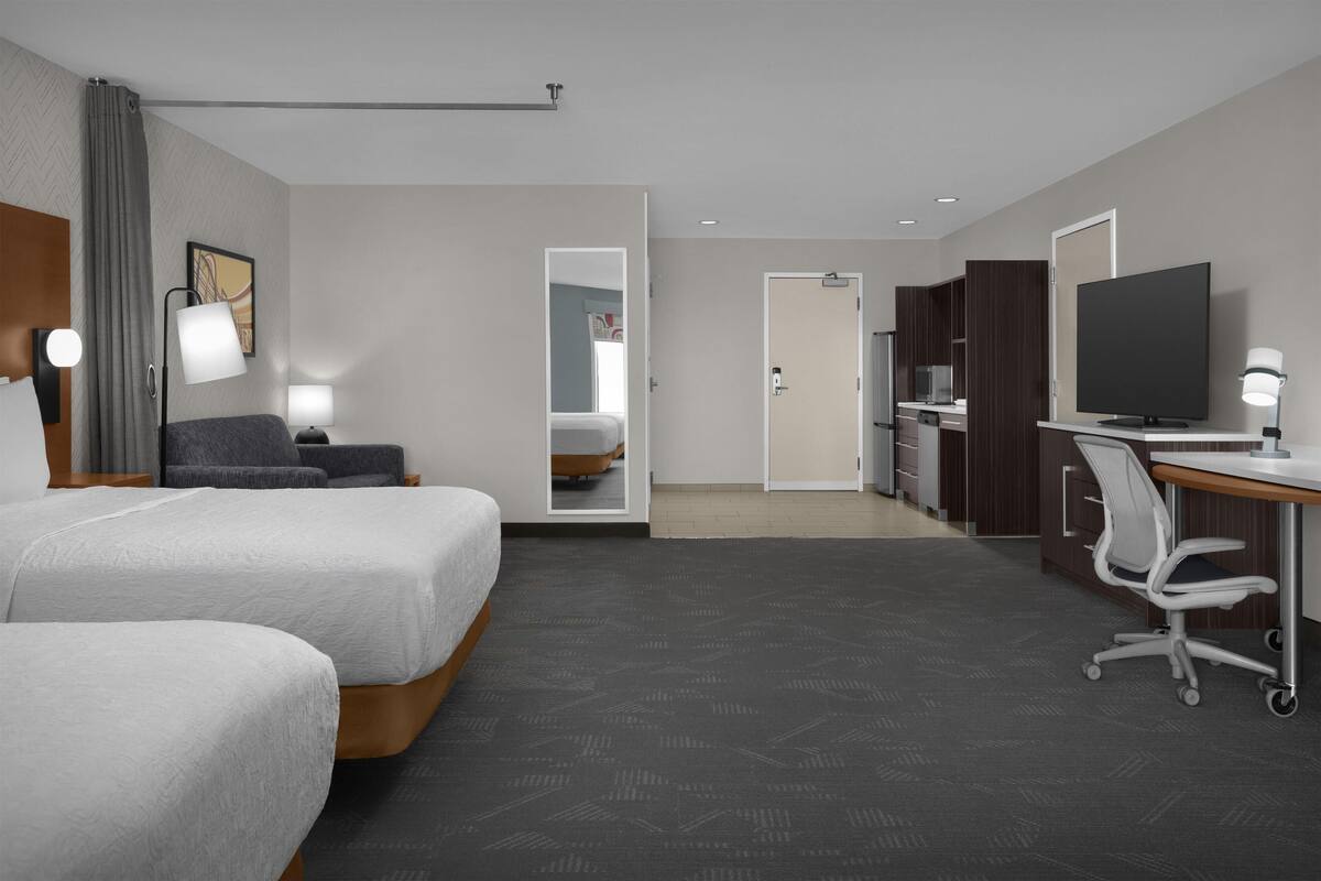 Een hotelkamer met twee bedden, een bureau, een stoel, een televisie en een badkamer zichtbaar door een geopende deur.