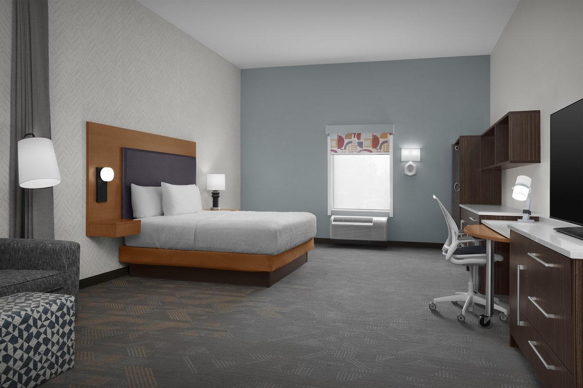 Een hotelkamer met een bed, nachtkastje, lamp, stoel, bureau, televisie en een raam.
