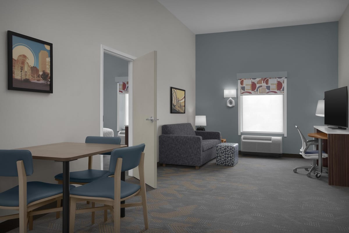Hotelkamer met een eettafel, stoelen, een bank, een televisie, een lamp en een raam met gordijnen.