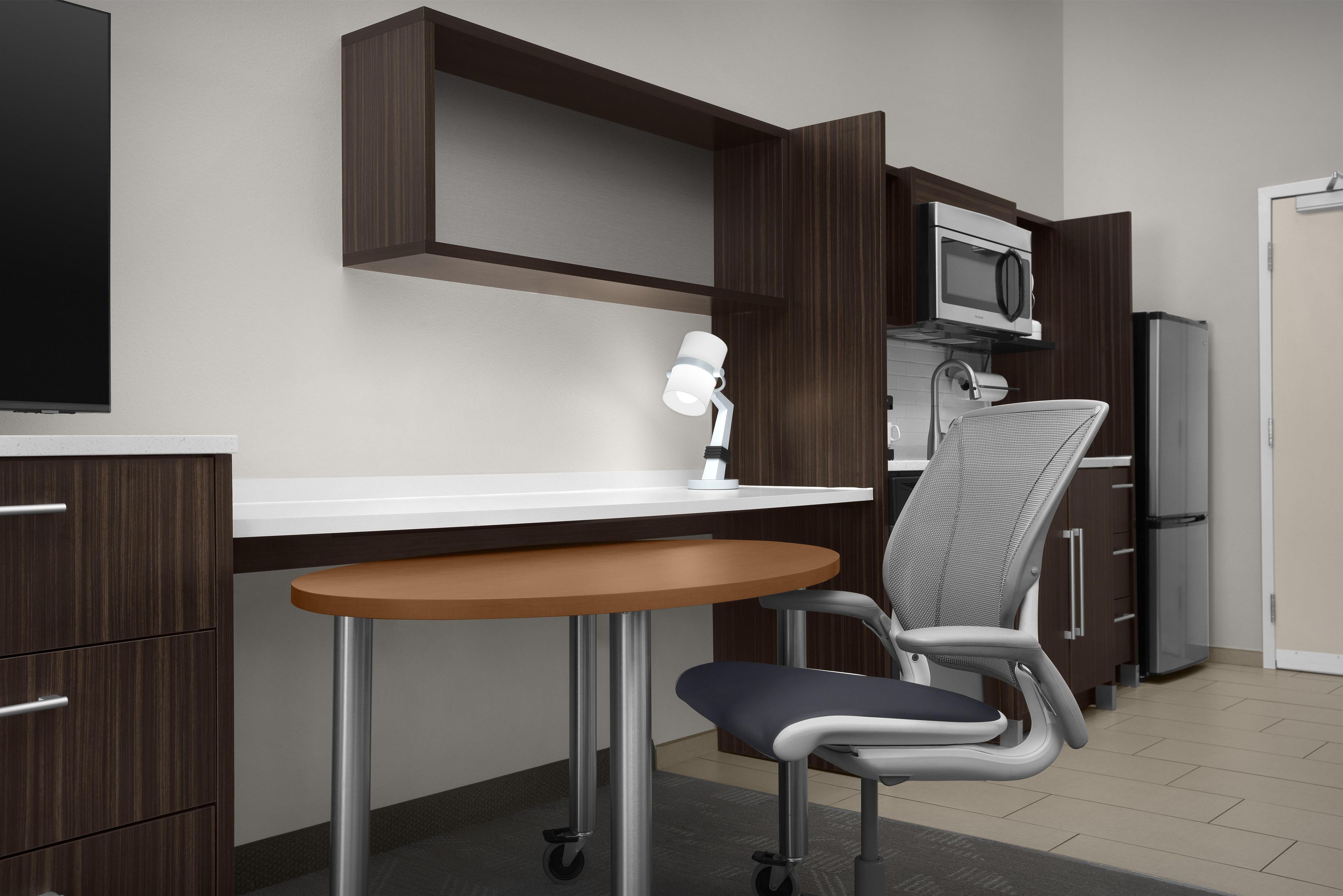 A modern kitchen with a microwave, refrigerator, and a dining area with a table and chair.