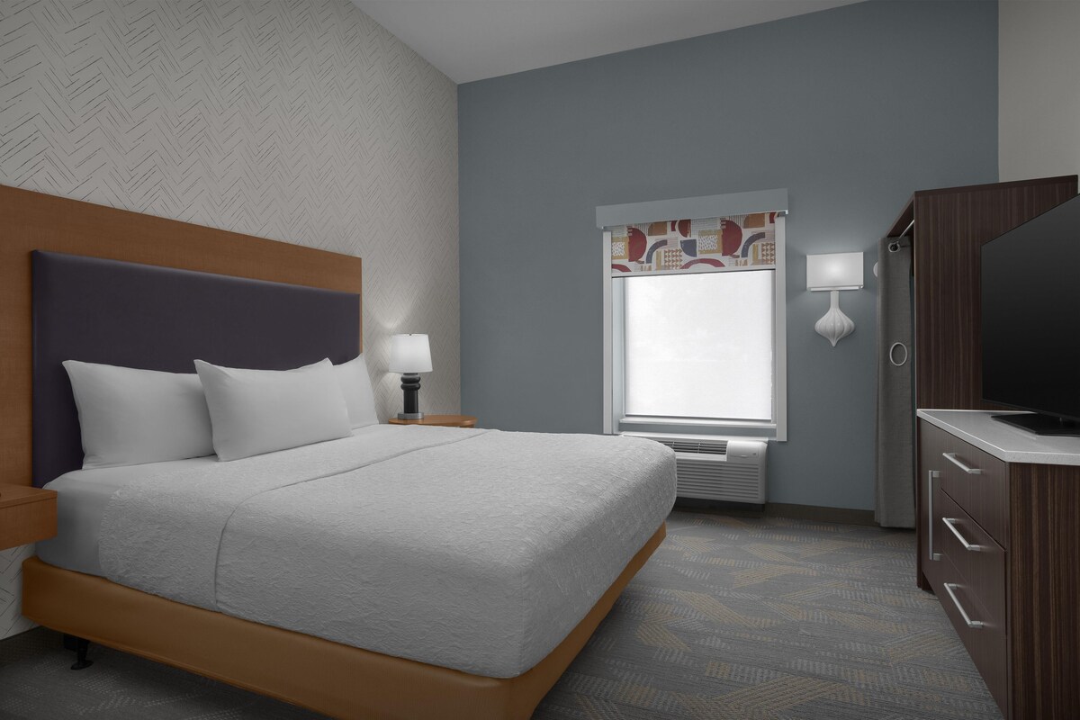 Hotelkamer met een bed, nachtkastje, lamp, raam, airconditioning en een televisie.