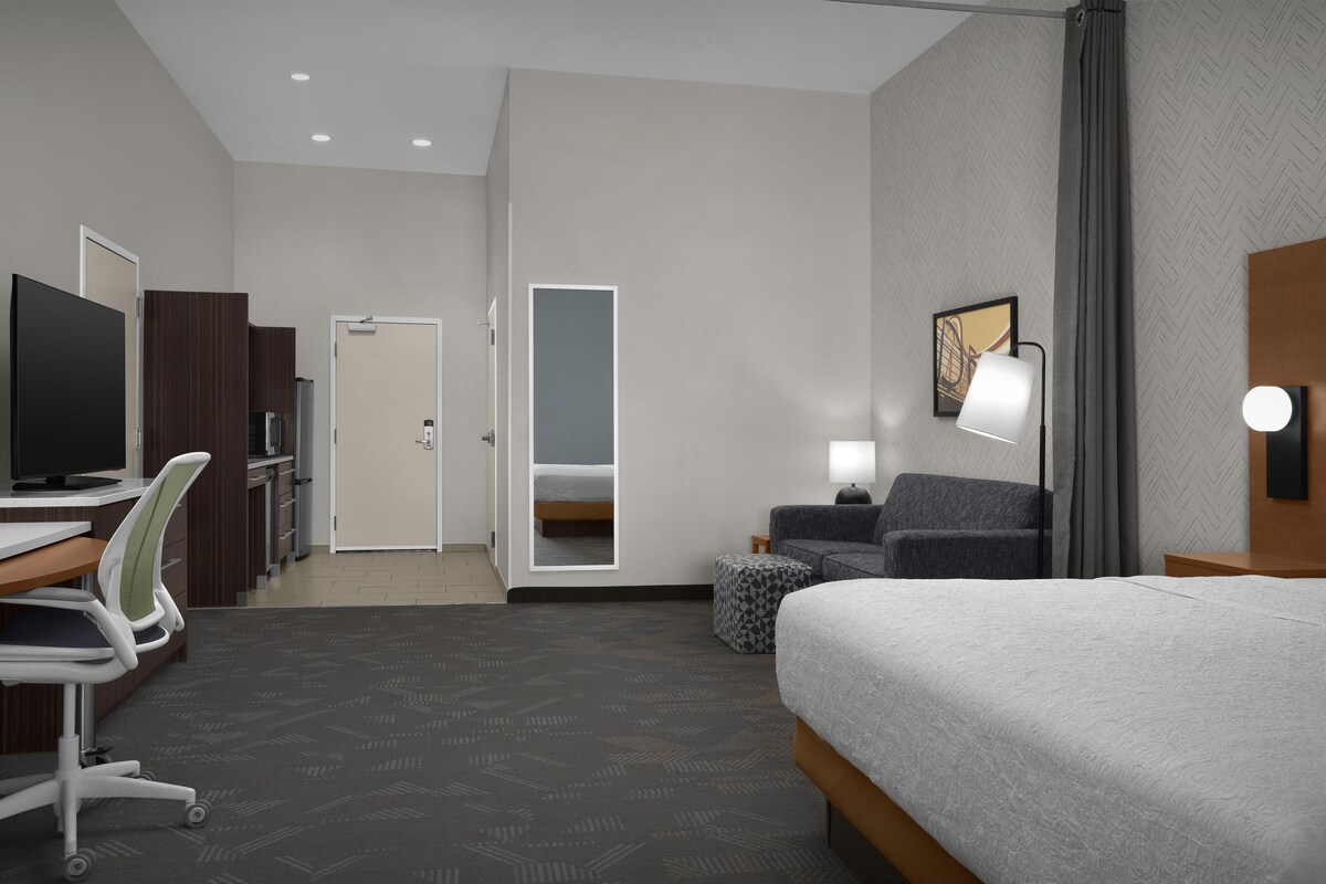 Een hotelkamer met een bed, bureau, stoel, televisie en een klein zithoekje met een lamp.