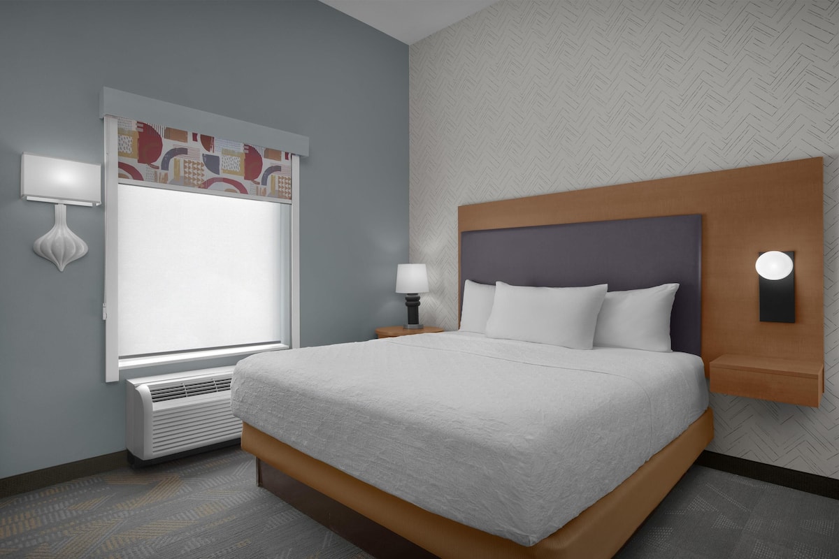Een hotelkamer met een bed, een raam, een wandlamp en een verwarming.