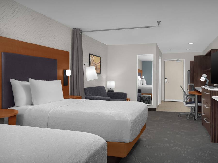 Ein Hotelzimmer mit zwei Betten, einem Schreibtisch, einem Fernseher und einem Badezimmer.