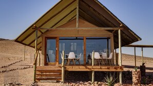 A wooden structure with a glass door, outdoor seating, and a desert backdrop. - Kanaan N/a'an ku sê Desert Retreat (Kanaan)