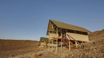 A desert-style building with a flat roof, wooden staircase, and a patio area.